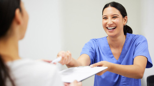 Smiling dental receptionist in blue scrubs handing paperwork to a patient at a dental practice